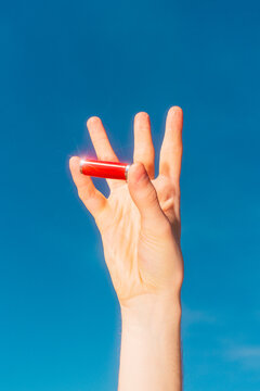 Hand holding red alkaline battery against blue sky