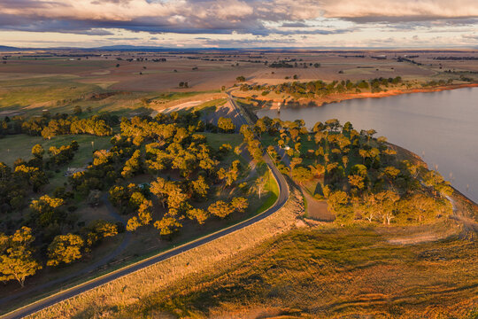 Golden light over a winding road over a reservoir embankment and trees