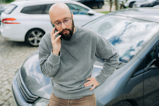 Serious man talking on smartphone beside parked car