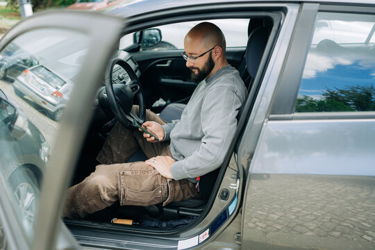 Relaxed man sitting inside parked car using smartphone