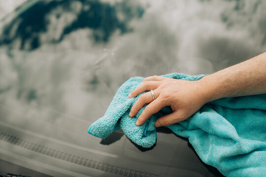 Male Hand Wiping Car Windshield with Blue Cleaning Cloth