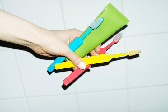 Hand holding toothbrushes and toothpaste in bathroom tile wall