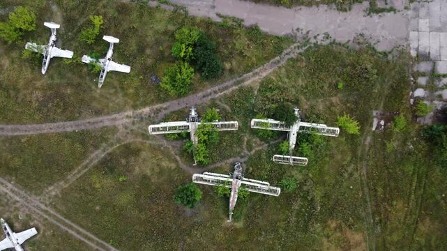 Aerial look down on weathered An-2 Antonov and trainer Aero L-29 airplanes abandoned in old airbase field, aviation remains in greenery
