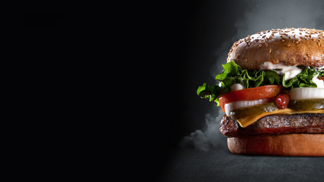 Juicy cheeseburger with lettuce, tomato, and onion on a dark background.