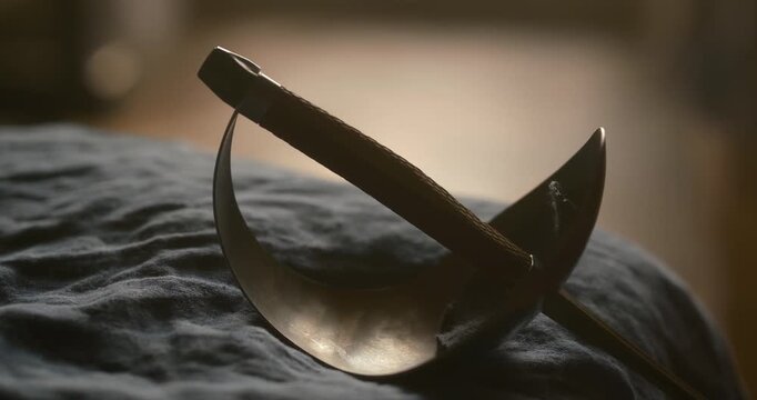 Cinematic Fencing Sword with Bell Guard on Dark Fabric. Dramatic warm side lighting creates striking highlights and deep shadows. Shallow depth of field with beautiful bokeh background.