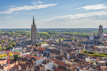 Obraz premium Bruges town in Belgium, Europe. Panoramic Aerial View of a Historic European Cityscape with Ancient Towers and Red Rooftops Under a Bright Blue Sky