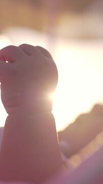 Vertical footage of slow motion close-up shot of baby girl lying on back in bassinet and moving hands. Shot in warm evening sun light