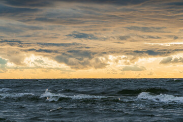 Obraz premium Dramatic ocean waves under a stormy, golden sunset sky