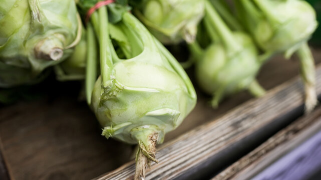 Green kohlrabi bulbs and leaves resting in a wooden crate at a market