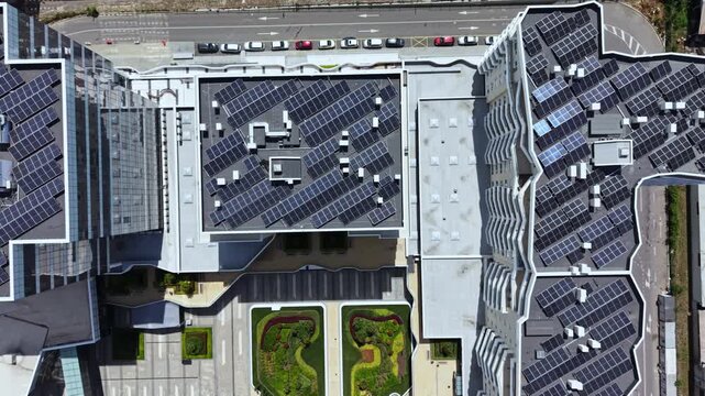 The scene shows multiple buildings equipped with solar panels on their roofs. Below is a garden area with grass and plants. The setting is in a city with clear skies.