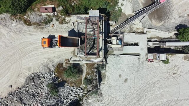 Trucks transport stone materials at a granite quarry site with machinery and a processing area working on the extraction and production process during daylight hours.