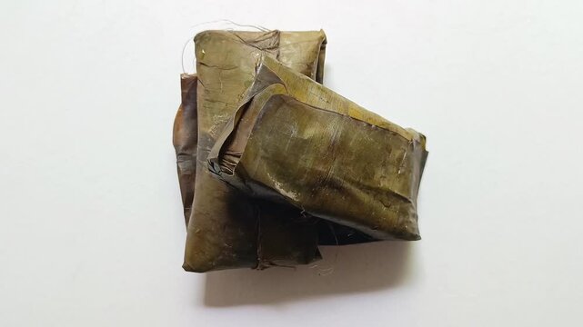Studio shot of two traditional Guatemalan chaya tamales made with Cnidoscolus aconitifolius leaves stacked over a rustic plantain leaf isolated on white background in Peten, Guatemala.