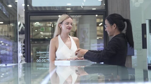 Side view of a female optical shop worker in uniform carefully fitting glasses for a blonde customer. Concept of retail customer service, personalized eyewear consulting, and professional vision care.