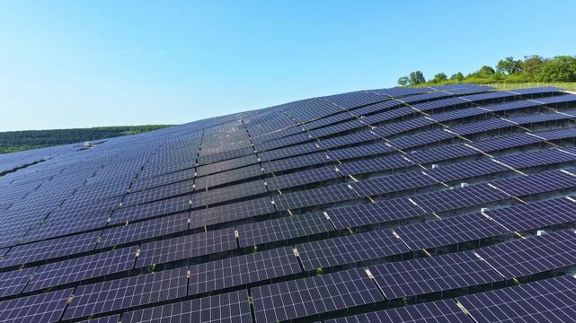Rows of solar panels cover a sloped area under a blue sky. The panels reflect sunlight and contribute to renewable energy generation. The scene shows a modern energy solution.