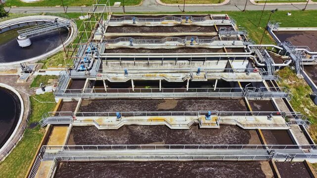 Aerial sewage treatment basins with clarifiers, rectangular aeration tanks and parallel channels, extensive piping and valves, maintenance walkways, green