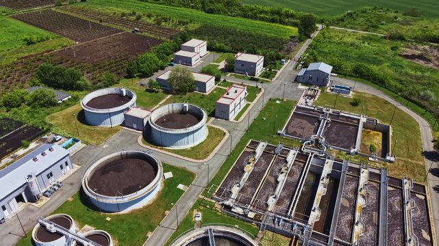 Wide aerial wastewater plant amid farmland showing circular clarifiers and sedimentation basins, sludge digesters, service buildings, access roads, stormwater