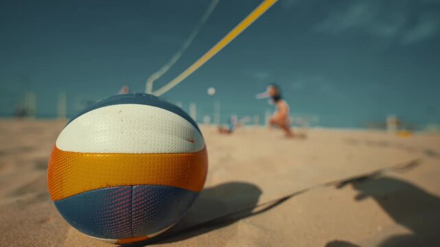 Beach volleyball game at sunset with players and a focus on the ball in the sand