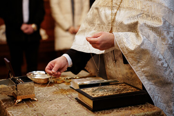 Religious ceremony priest holding christening cross and holy water in church during ritual. Eastern Orthodox baptism, christian blessing, sacred sacrament, religious ritual event © Olga Yashnikova