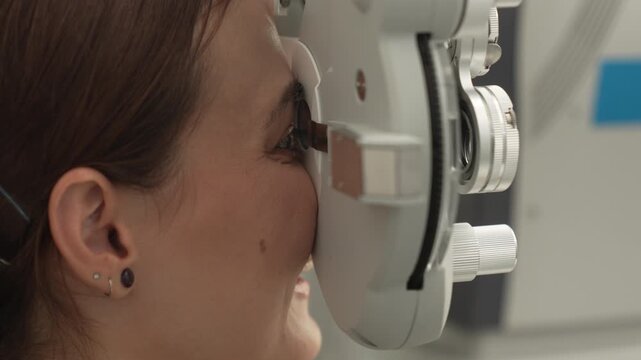 A positive female patient undergoes a professional vision check and refraction test using advanced ophthalmic equipment. This high-value commercial stock imagery represents preventative healthcare, pr