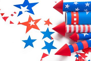 Fototapeta premium Fourth of July USA Independence Day festive celebration concept with copy space. Handmade craft paper rockets decorated with stars and stripes, clapper and confetti, white background.