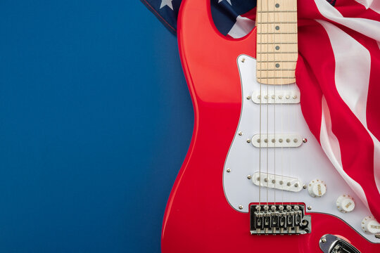 Red electric guitar with American flag on blue background. Patriotic music concept inspired by rock culture, live performance and American entertainment with copy space