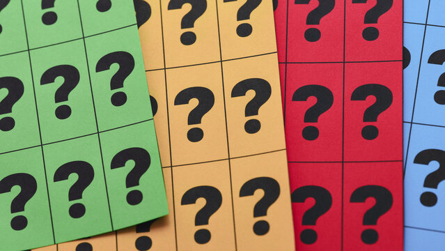 A close-up shot of colorful paper sheets divided into grids with printed black question marks.