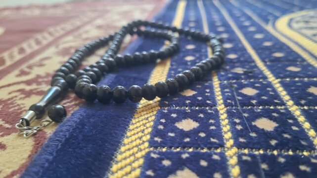 Black prayer beads resting on a patterned islamic prayer rug