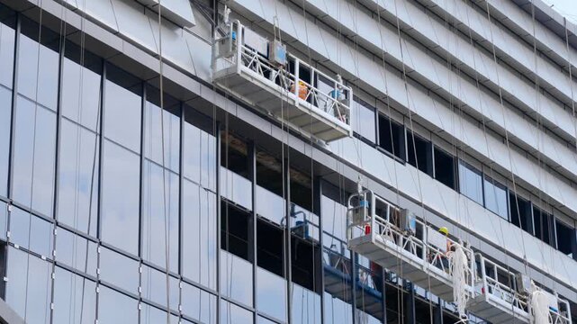 Construction workers on suspended platforms installing panels on modern building facade