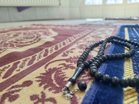 Black prayer beads resting on a patterned islamic prayer rug