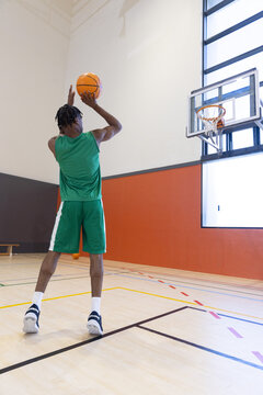 Male basketball player is preparing to shoot toward hoop on polished hardwood court near window
