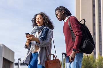 Diverse friends checking smartphone while standing at transit hub with wheeled suitcases handbag © wavebreak3