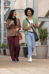 Fototapeta premium Diverse coworkers wearing smart casual walking by office building on path holding coffee and bags