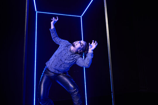 Young woman with short hair posing dynamically inside neon blue light cube in dark studio