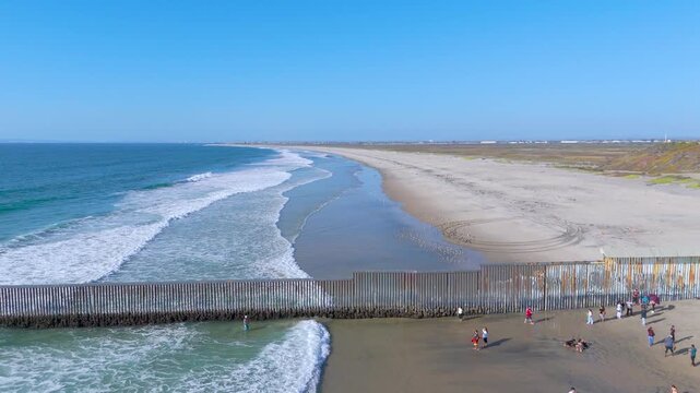 Aerial High Angle View of Coastal Border Wall Infrastructure and Pacific Shoreline in Tijuana, Mexico. The video highlights the massive vertical steel posts of the international border fence.