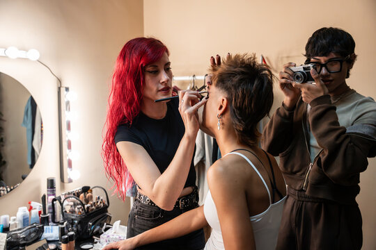 Makeup artist applying eyeliner next to photographer at backstage
