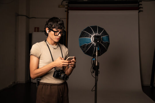 Photographer checking smartphone beside studio softbox light