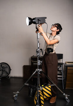 Photographer adjusting studio light on stand in photo set