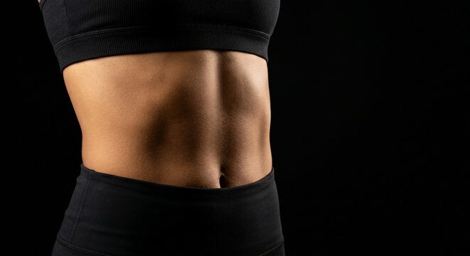 Close up of fit woman muscular belly on black background