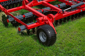 Obraz premium Red agricultural disc harrow rests on lush green grass