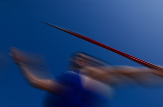 Track and field athlete throwing a javelin, fast action sport photography with motion blur, powerful spear throw under clear blue sky background