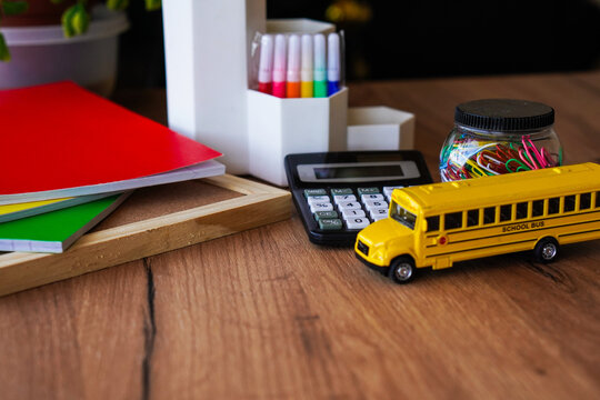 School bus toy on wooden desk with calculator notebooks markers and paper clips for back to school theme math learning classroom supplies homeschool workspace and colorful education background concept