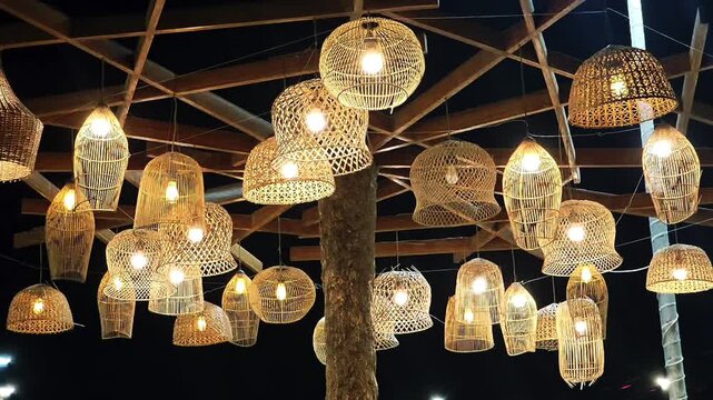 Warm boho bamboo and rattan pendant lamps glowing under a tropical wooden canopy at night. Perfect for rustic cafe ambiance, resort decor, and sustainable lighting design.
