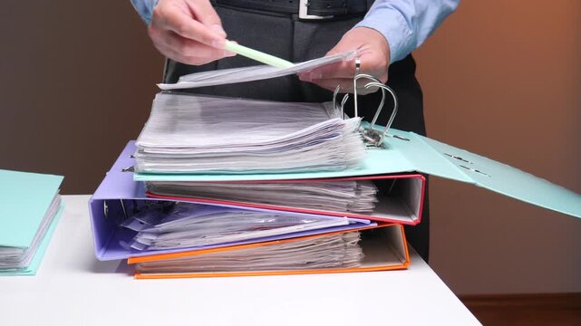Businessmans hands sorting important paperwork in colorful ring binders on a desk, depicting office administration, filing, data management and financial record keeping processes