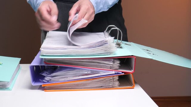 Business professional hand searching through important paperwork and documents in a colorful ring binder, demonstrating office management and organization of data