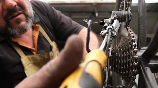 Camera filming bicycle mechanic adjusting sprocket position with screwdriver and turning pedals by hand with bicycle turned upside down. Professional repair and adjustment of bicycle components