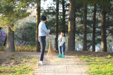 Obraz premium Mother and child share gentle, playful moment. Sunlight glows through tall pine trees. Child holds small shovel, eyes full of joy. Mother laughs softly, guiding child's efforts
