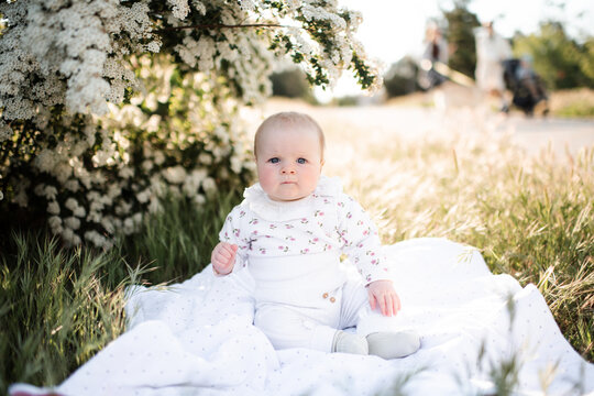 Cute baby girl with frowning face sitting on green grass lawn in park outdoors. Looking at camera. Childhood. Summer season.