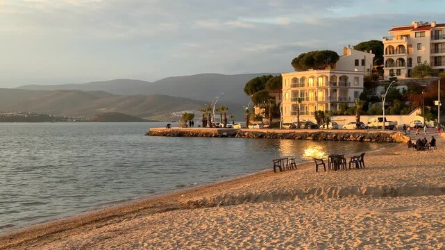 A warm golden hour view of the beach in Gulluk, Turkey. Seaside hotels, palm trees, and the calm Aegean Sea reflecting the low sunset light.