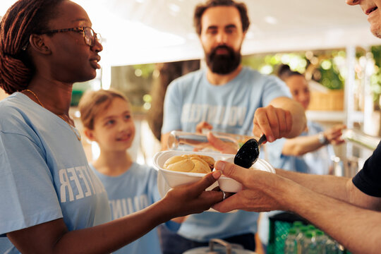 Friendly volunteers supporting the less fortunate by offering humanitarian aid through food distribution. Young people combating poverty by participating at outdoor hunger relief food drive program.