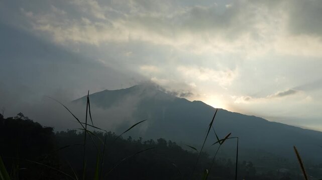 Beautiful time lapse of morning sunrise behind Mount Merbabu silhouette with rolling clouds and dramatic golden sky in Central Java.